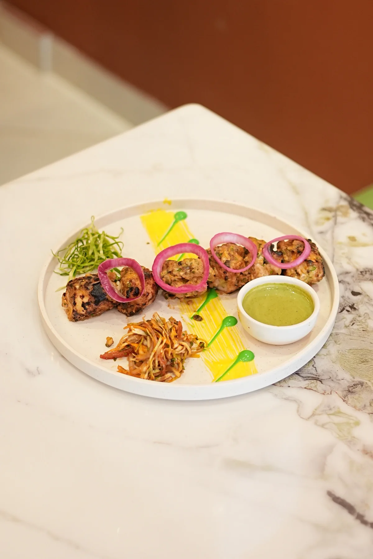 A grilled starter with onion rings, green dip and crisp garnishes on a white plate