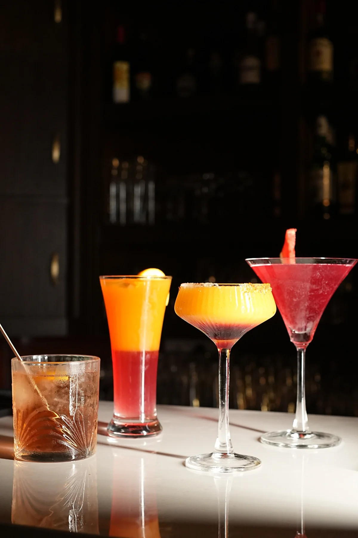 Four colourful cocktails in different glasses on the marble bar at RHYTHM