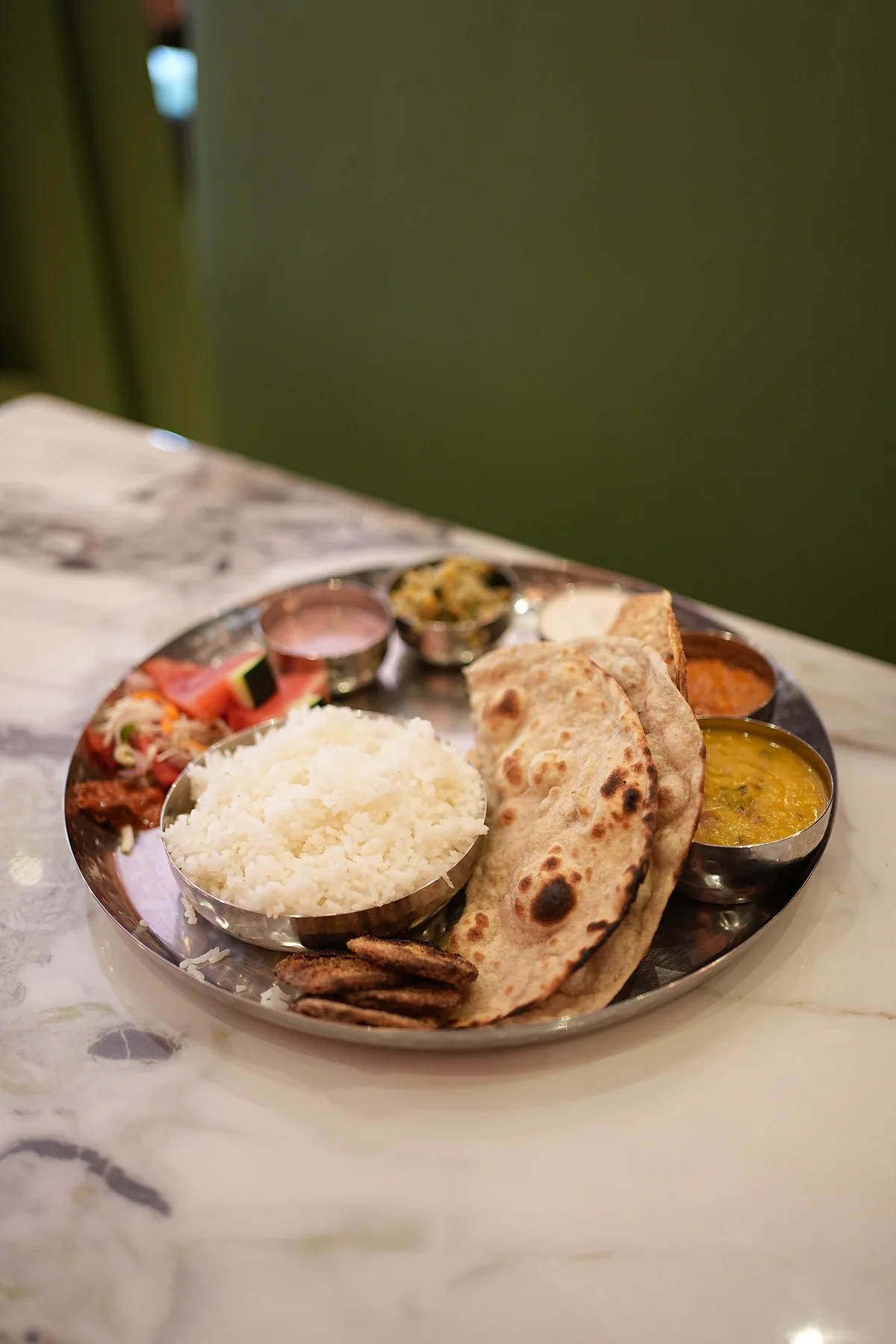 A thali with rice, bread and accompaniments on a marble table.