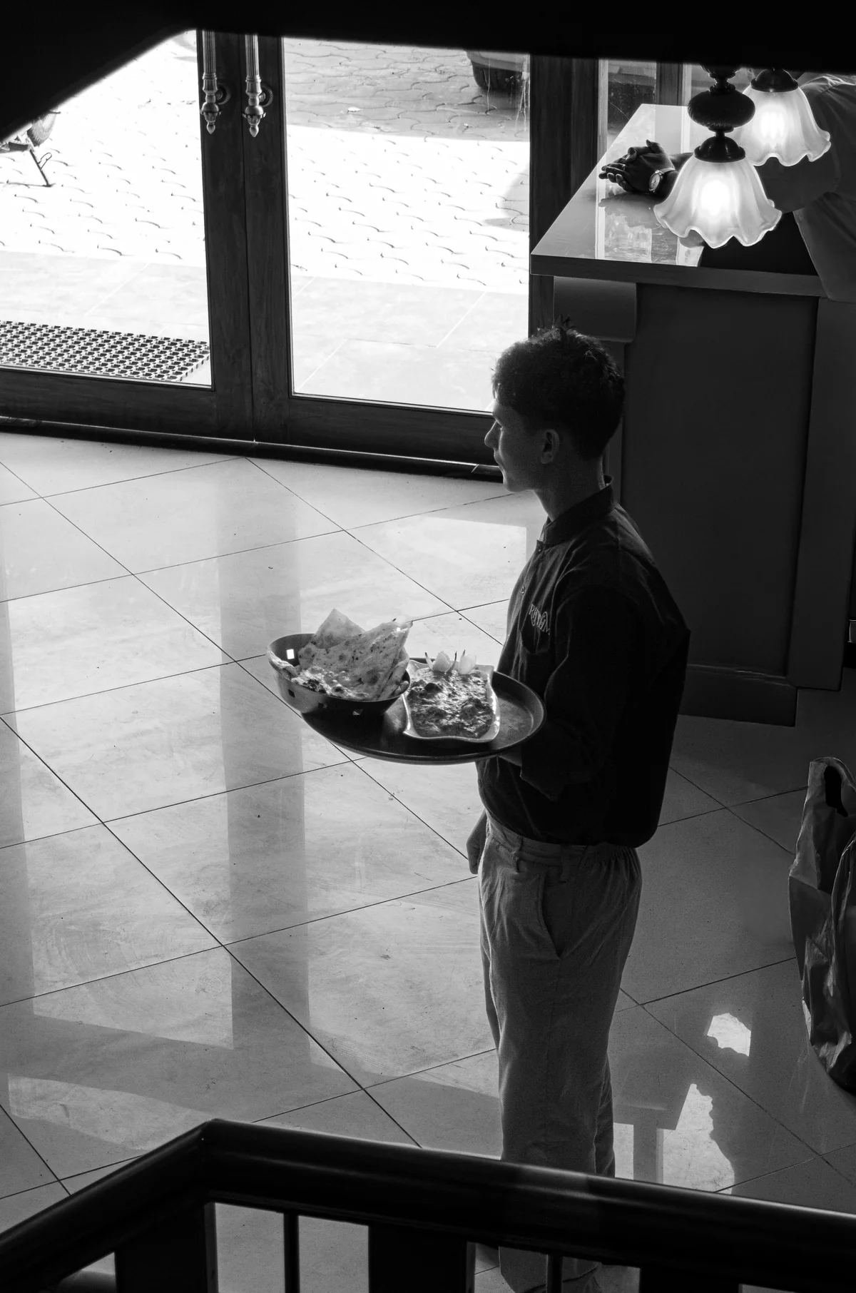 A black-and-white photograph of a member of the RHYTHM team carrying a meal through the restaurant